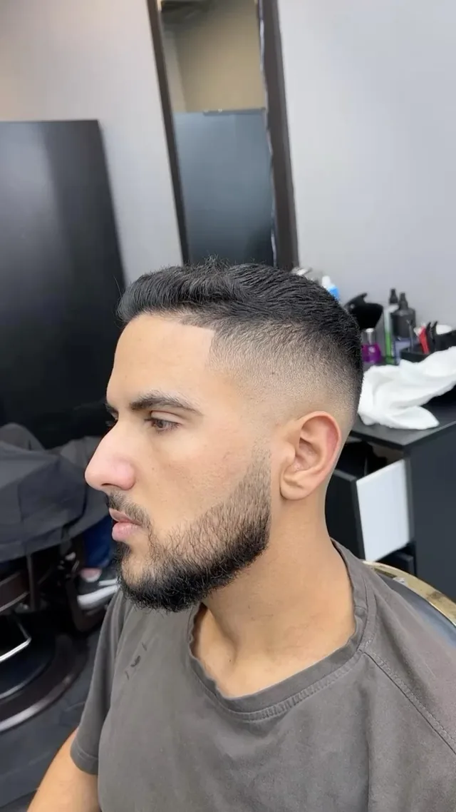 High skin fade with a short top and full beard, three-quarter view