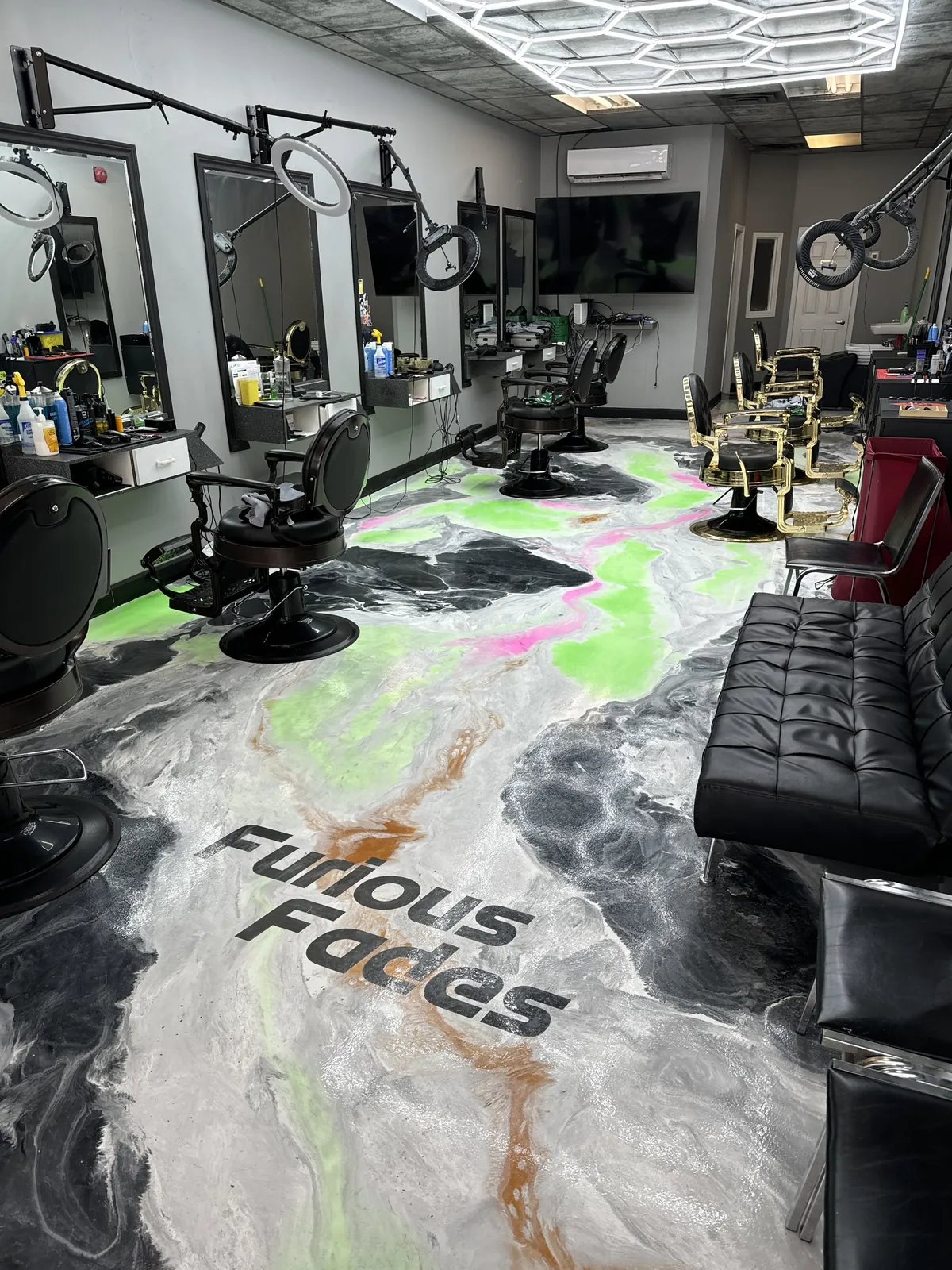 Inside Furious Fades barbershop: mirrors with ring lights, black and gold barber chairs and a marbled floor with the Furious Fades logo