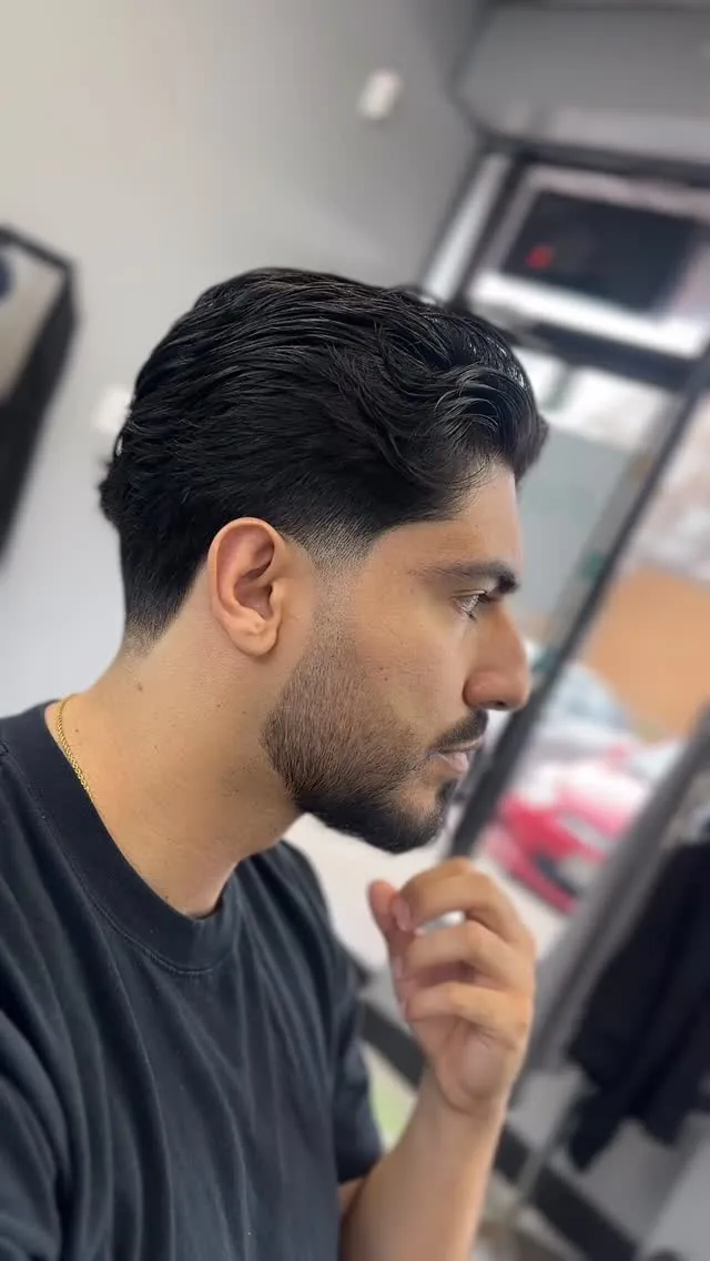 Slicked-back hair with a clean taper and shaped beard, side profile